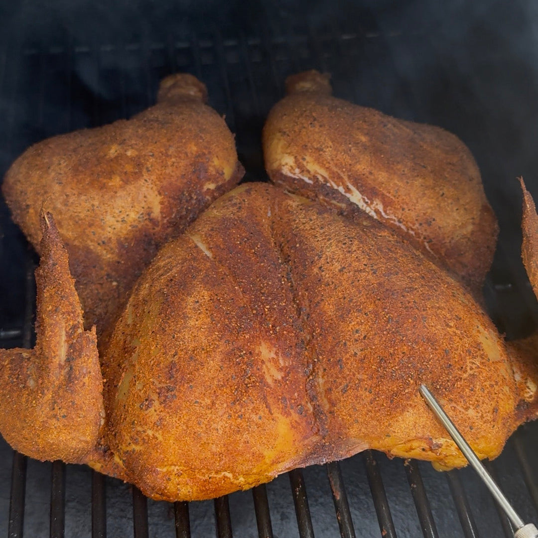 Chicken being grilled on a barbecue with a thermometer probe inserted.