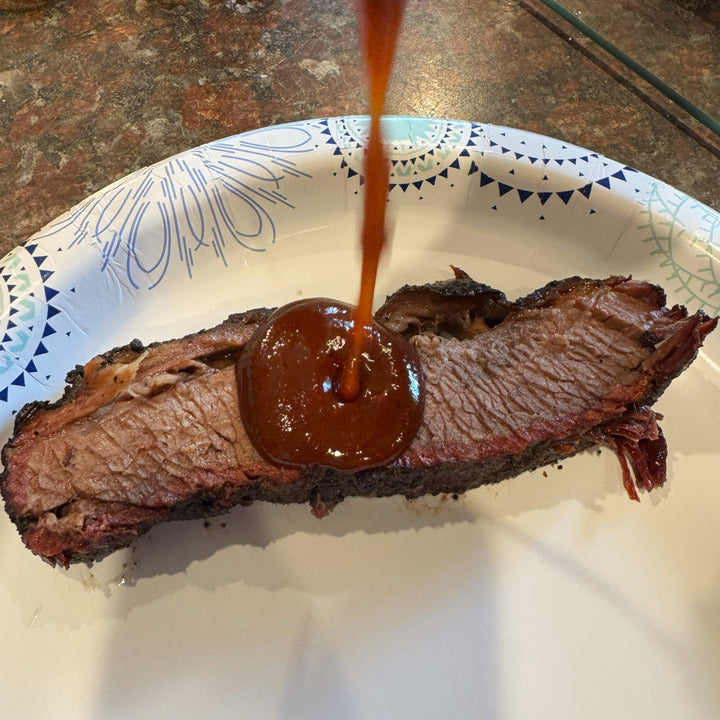 Spicy BBQ sauce poured over smoked brisket slice with bark and smoke ring using Barracks BBQ Blazin’ Battle sauce