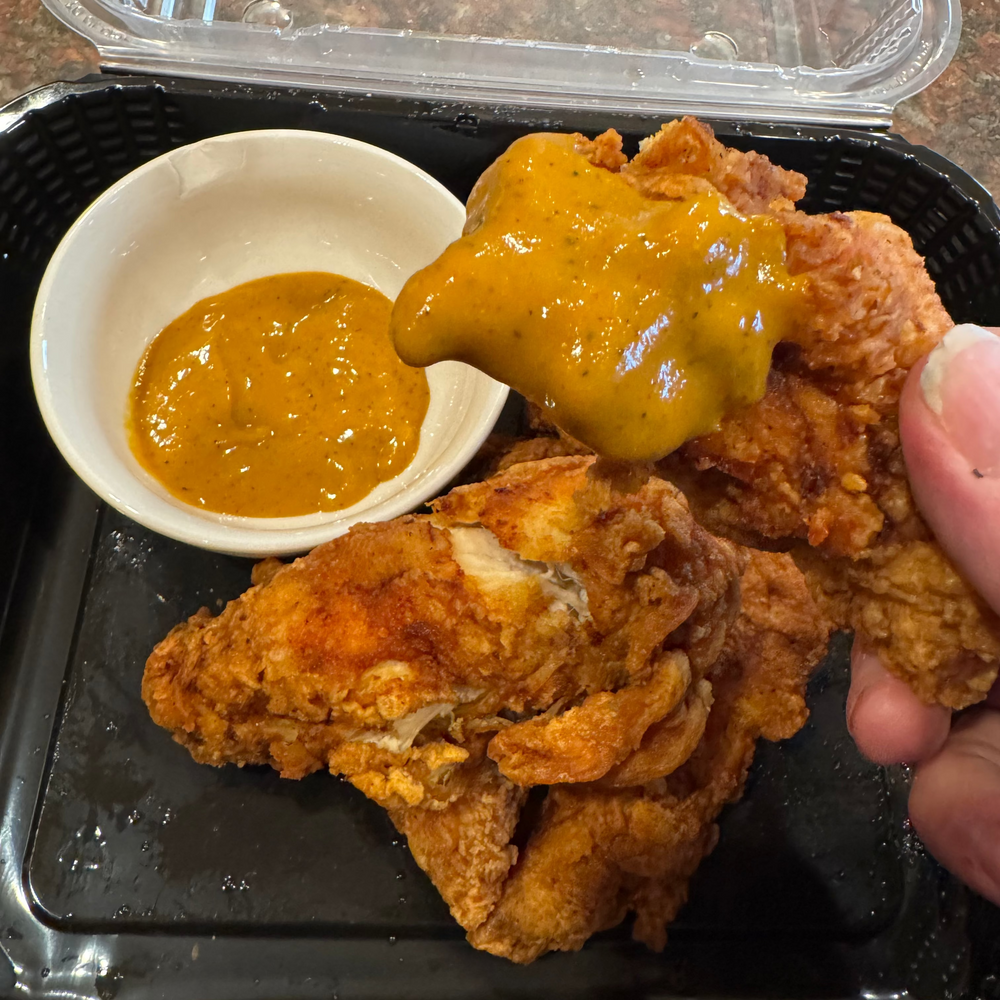 Fried chicken with a side of Mustard Gas BBQ sauce in a takeout container.