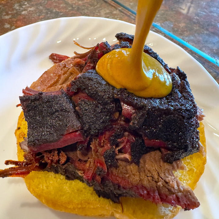 Creamy mustard BBQ sauce poured over smoked brisket sandwich with crispy bark and smoke ring using Barracks BBQ Mustard Gas sauce