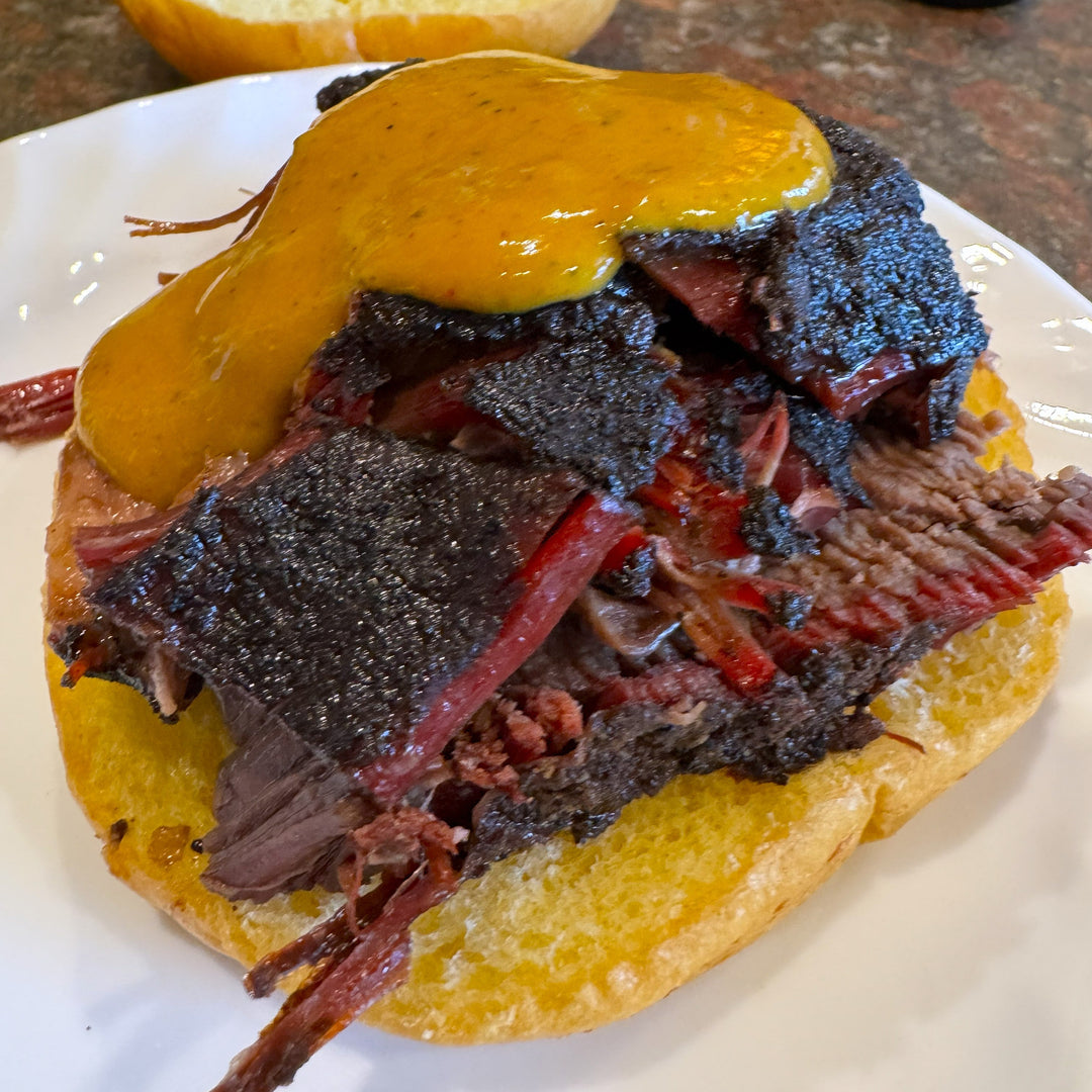 Smoked brisket sandwich topped with thick mustard BBQ sauce and crispy bark using Barracks BBQ Mustard Gas sauce